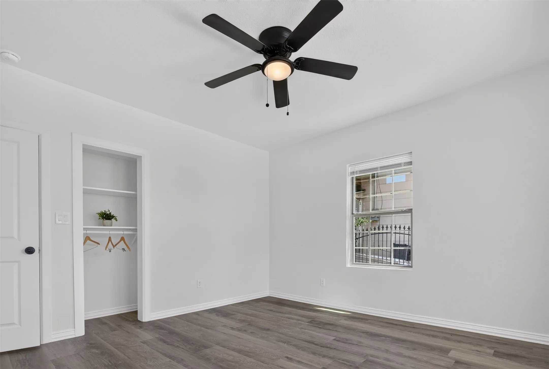 Wood-finish flooring, white walls, and a black ceiling fan with integrated lighting