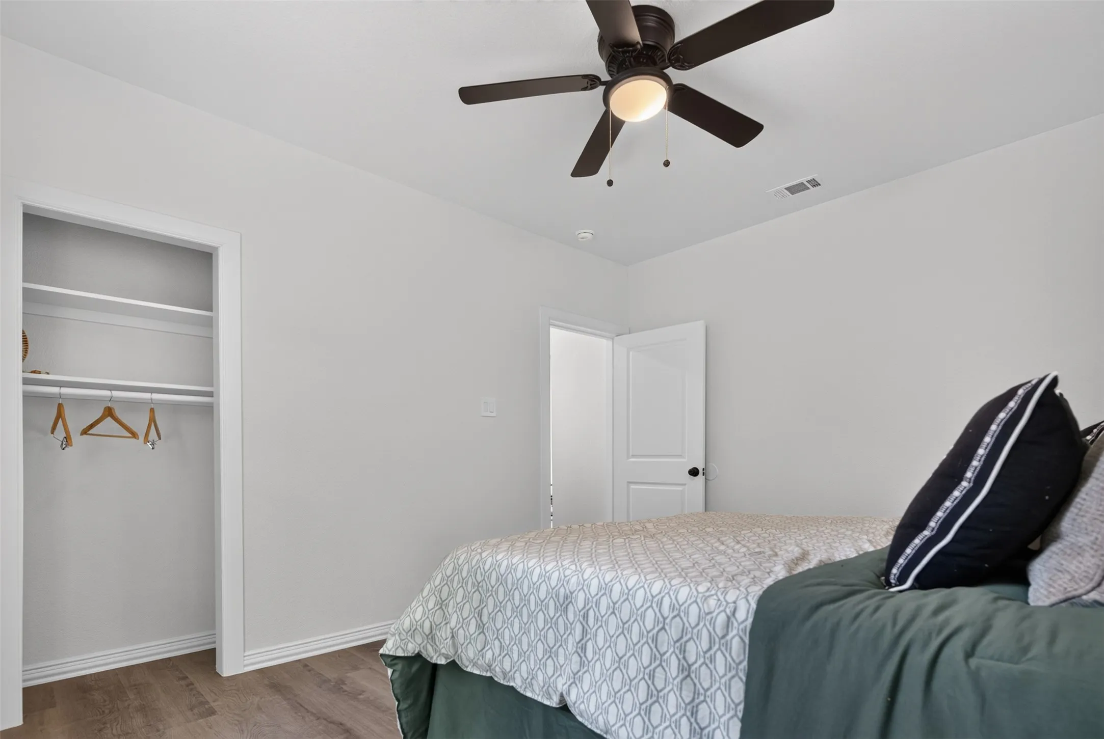 Bright secondary bedroom featuring a spacious walk-in closet with shelving and hanging rod, ceiling fan with integrated lighting, and wood-finish flooring throughout