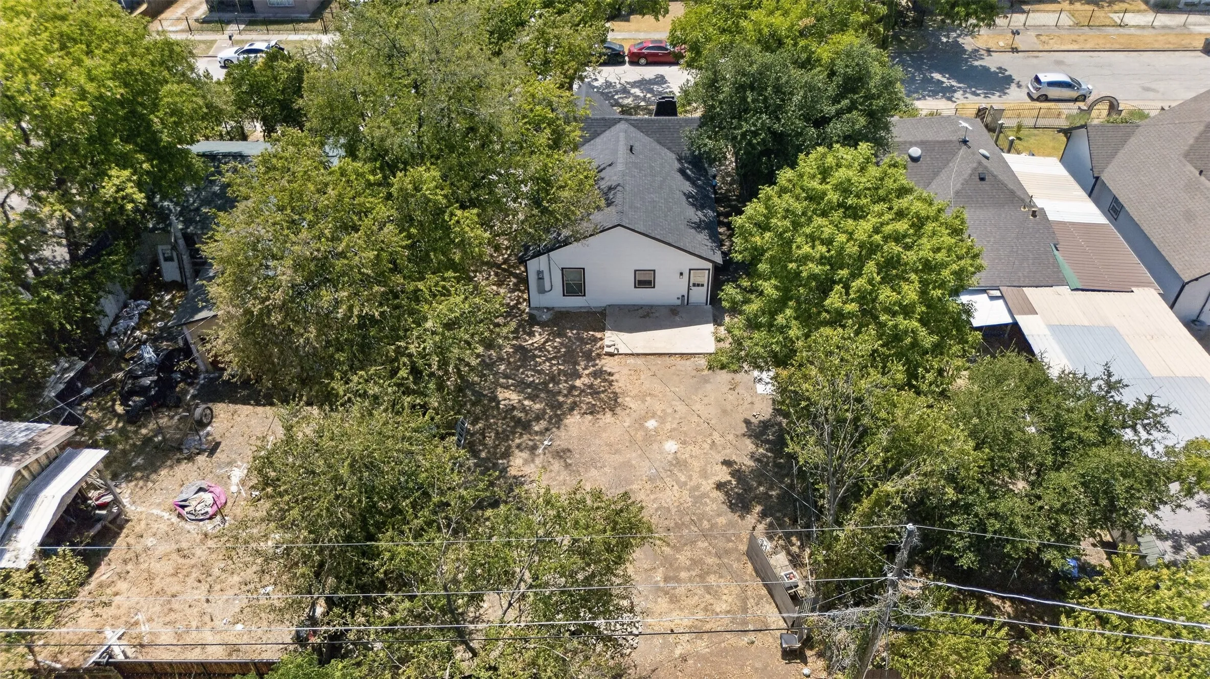 Aerial view showcasing a generous lot with mature landscaping, established trees providing natural privacy, and a single-story residence with updated roofing