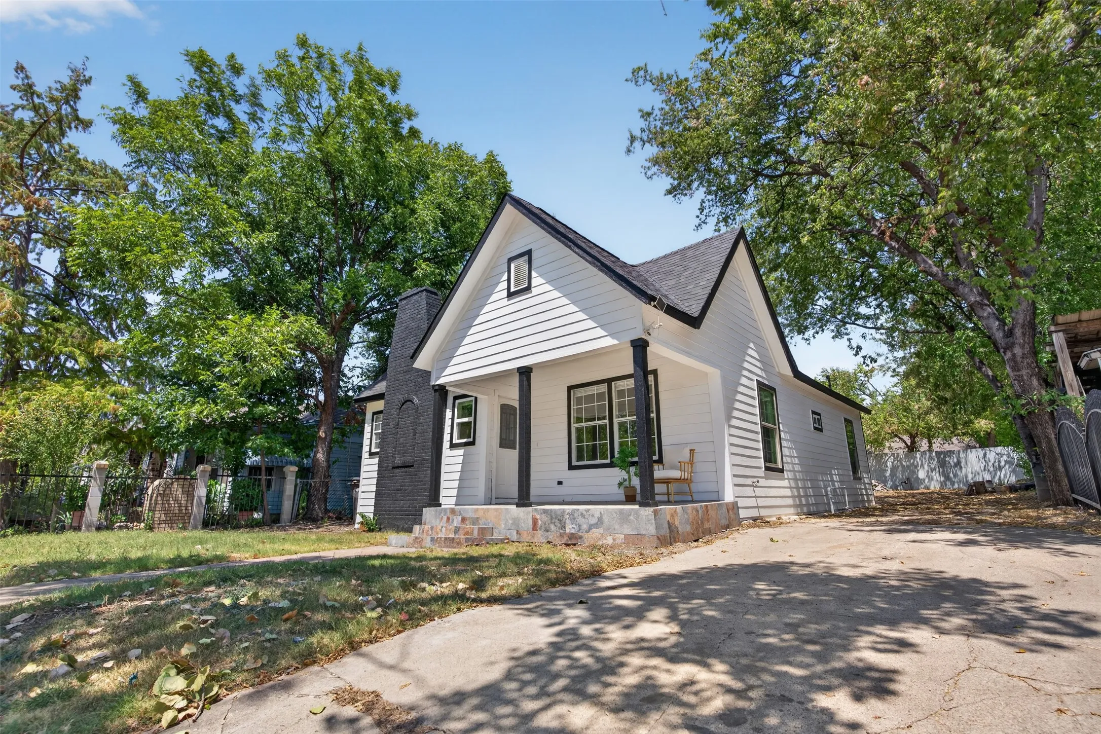 Charming cottage-style home featuring white horizontal siding, a distinctive peaked roofline with dark accents, and multi-pane windows