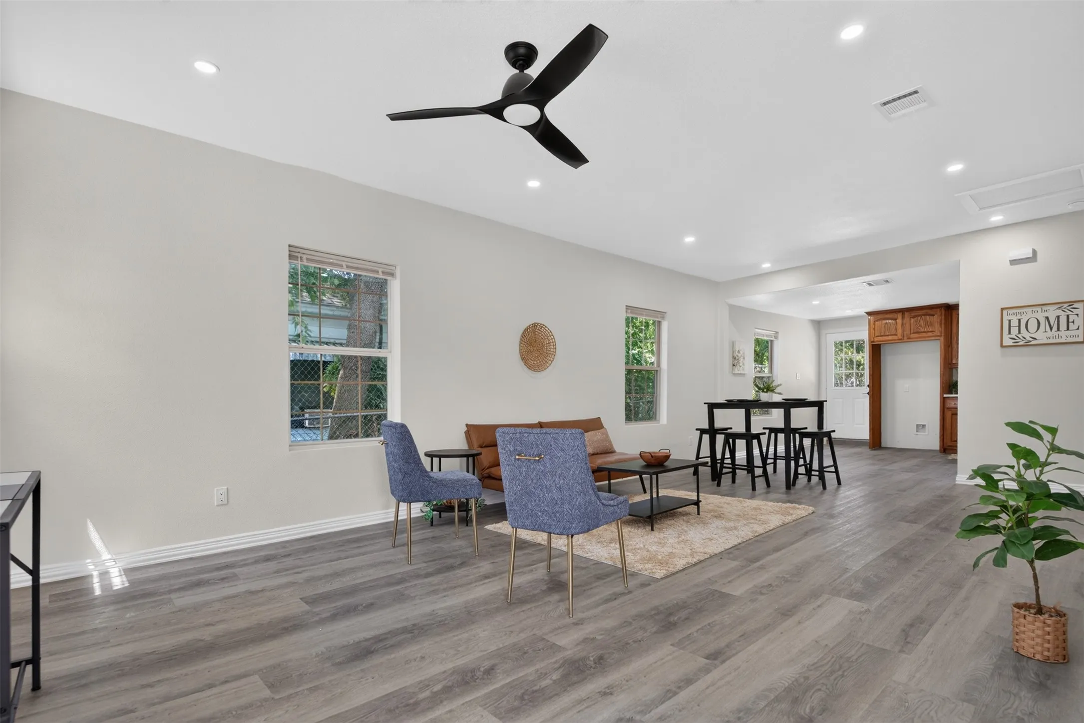 Spacious open-concept living area featuring wide-plank wood-finish flooring, recessed ceiling lighting, and a modern ceiling fan