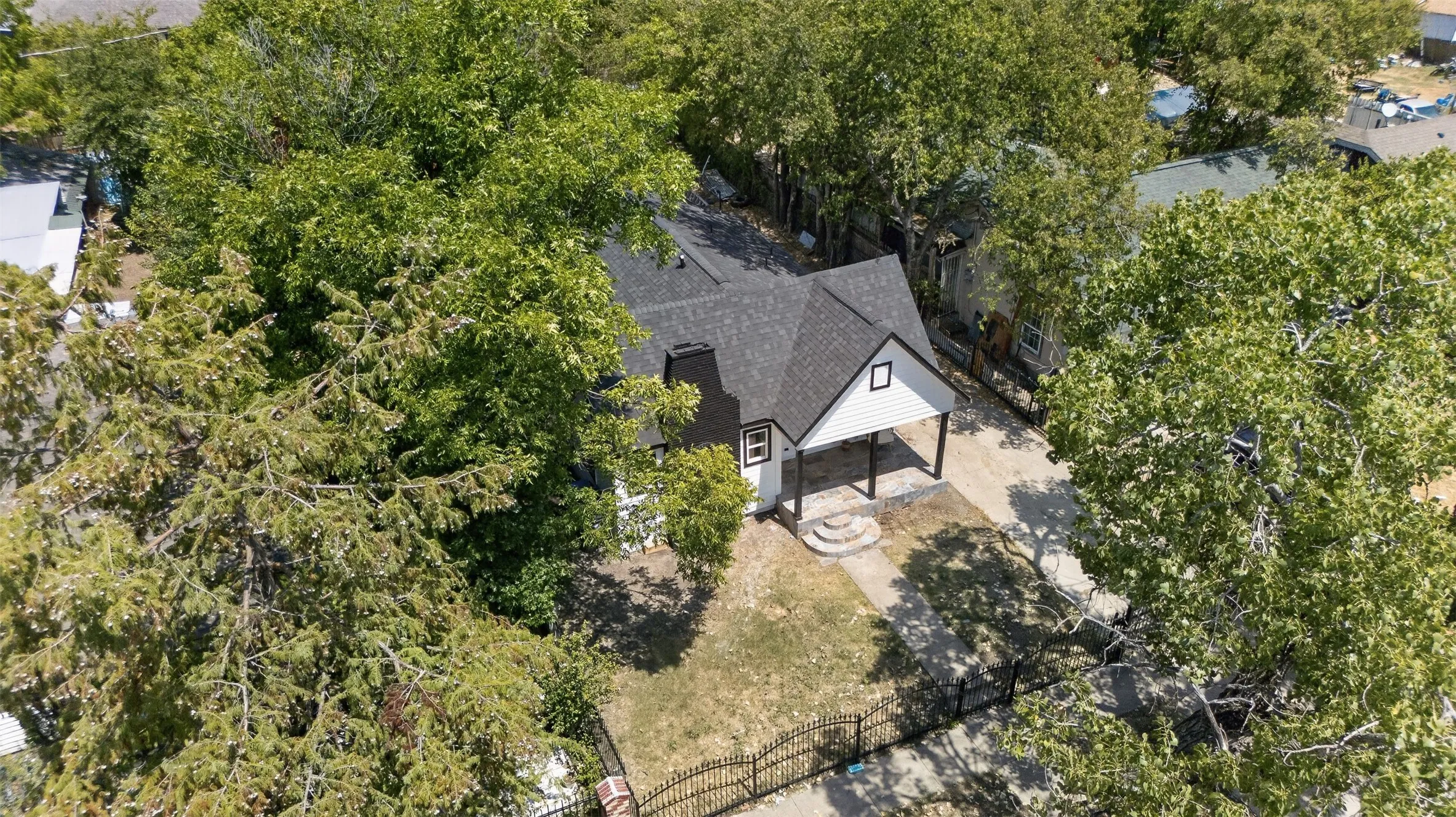 Charming cottage nestled among mature trees, featuring a gabled roofline, board-and-batten siding, fenced yard perimeter, and expansive tree canopy providing natural privacy and shade throughout the property
