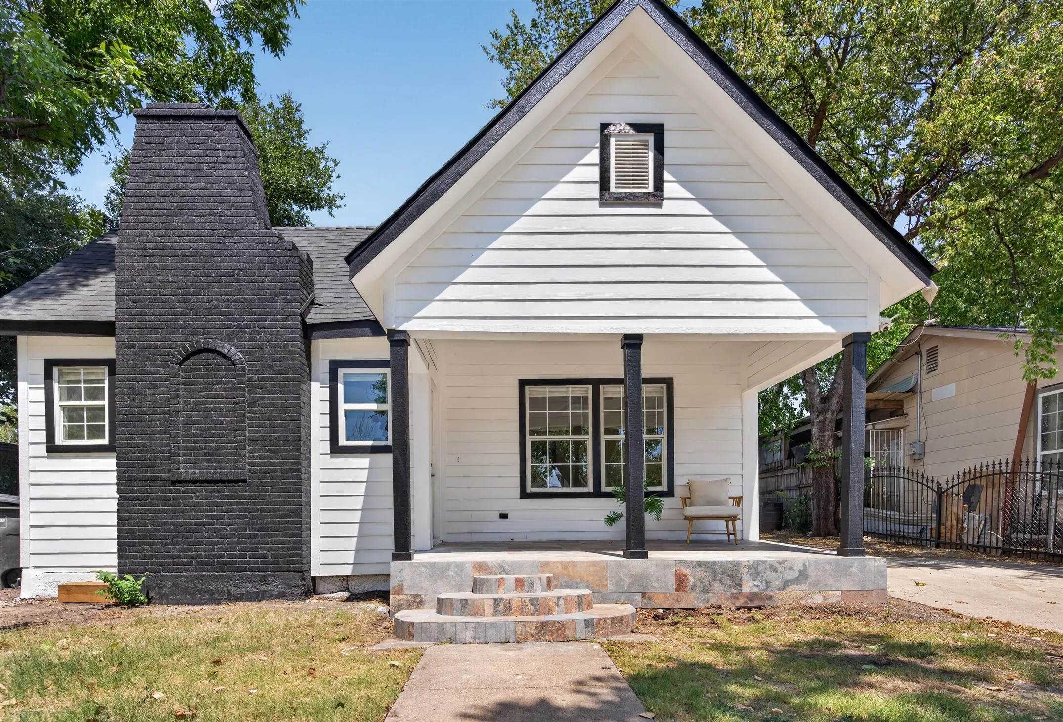Charming cottage-style home featuring a gabled roofline with peaked dormer, horizontal lap siding in soft cream tones, and a striking dark brick chimney