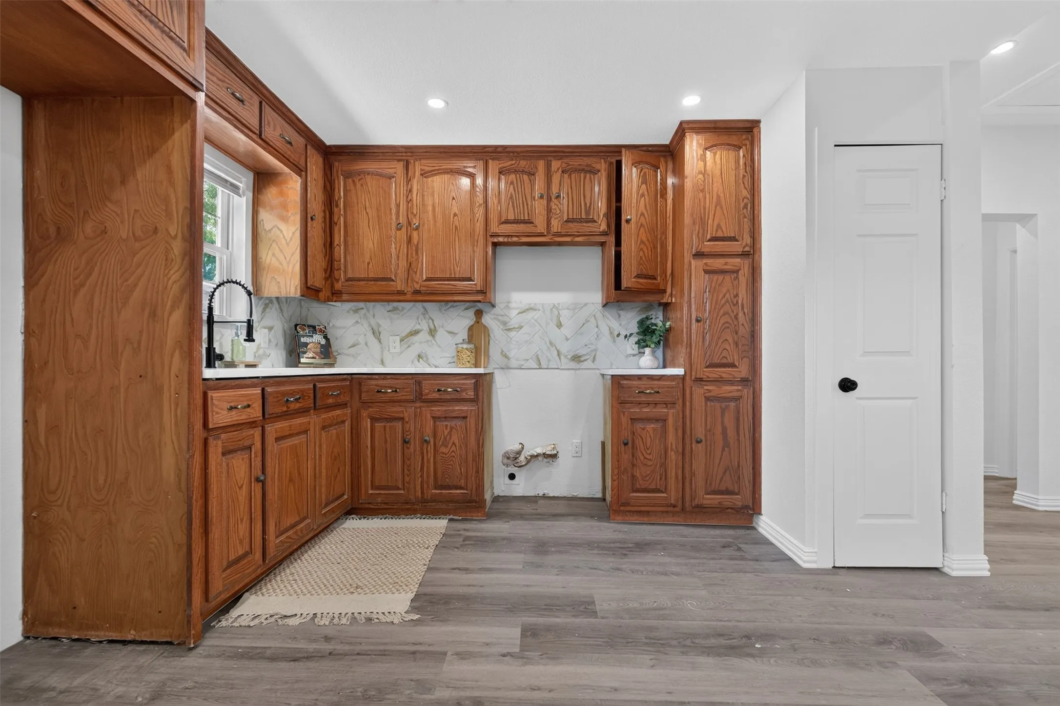 Wood-finish cabinetry with brass hardware, white countertops, and a patterned backsplash