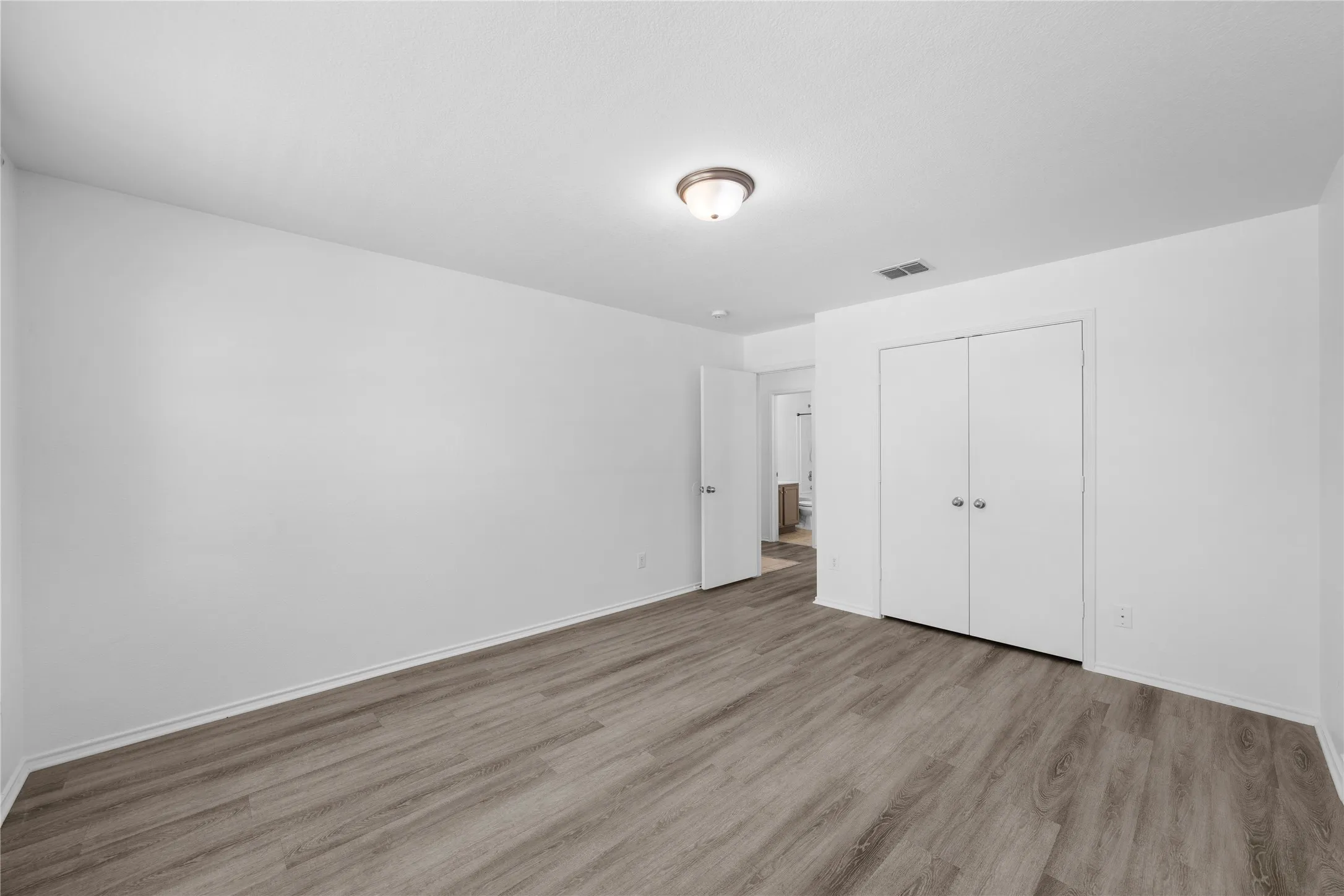 Wood-finish flooring, flush mount ceiling light, white bi-fold closet doors, white interior door