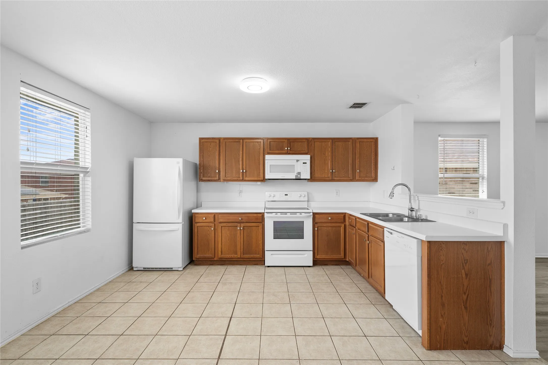 Kitchen featuring tiled flooring, wood cabinetry, white countertops, and white appliances