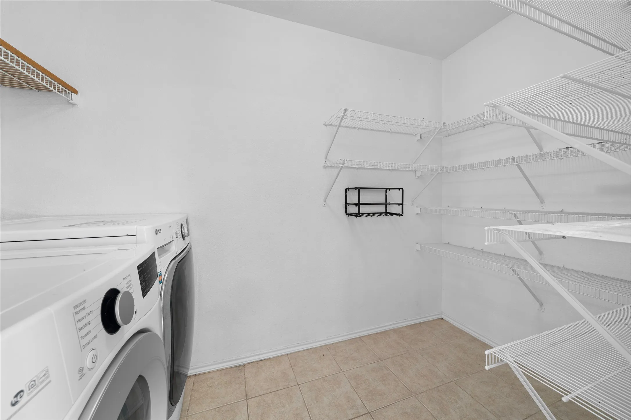 Dedicated laundry room featuring front-load washer and dryer, tile flooring, wire shelving for ample storage, and a window for natural light