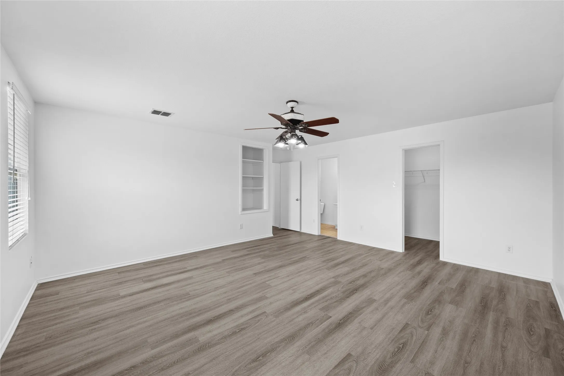 Spacious room featuring wood-finish flooring, a ceiling fan, and built-in shelving