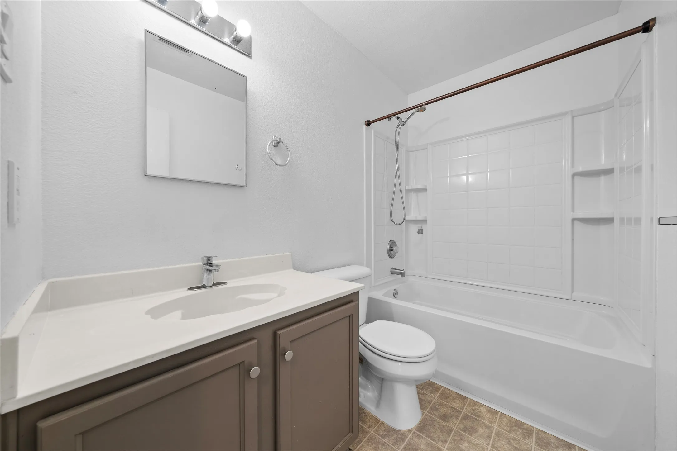 White tiled shower and bathtub combination with integrated shelving, a rectangular vanity mirror, and a single vanity with storage cabinets