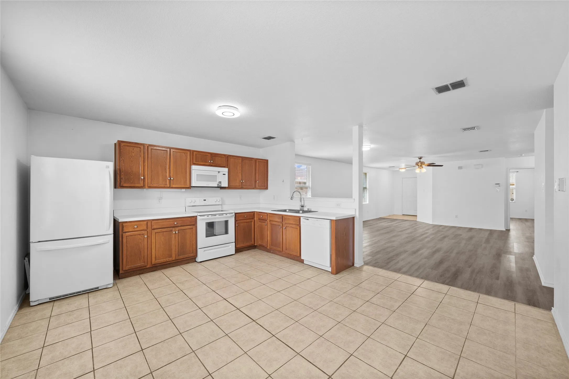 Kitchen featuring a full suite of white appliances, wood-finish cabinetry, light-toned countertops, and tile flooring
