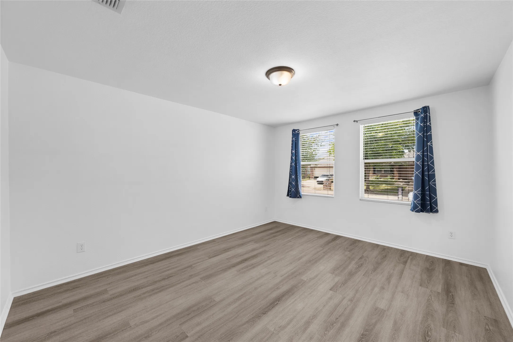 Wood-finish flooring, two windows, and a flush-mount ceiling light fixture