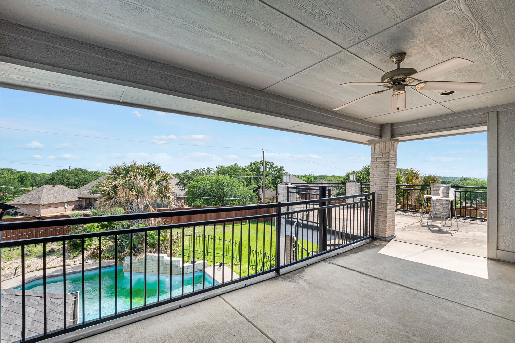 Expansive covered terrace with polished concrete flooring and ceiling fan, offering panoramic vistas of manicured grounds, resort-style swimming pool, and lush landscape