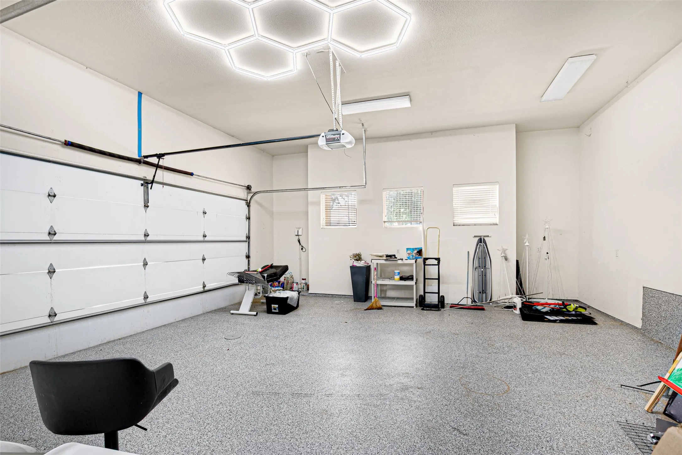 Epoxy-coated flooring, white panel garage door, hexagonal ceiling lighting, recessed windows with blinds, and white walls