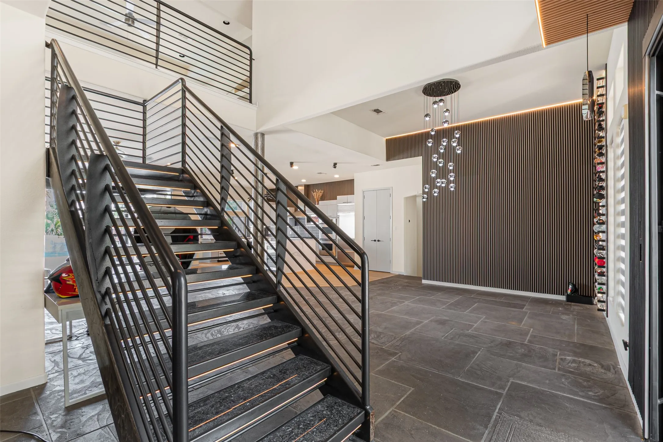 Open-tread staircase with metal railing, stone tile flooring, and a decorative wall panel with integrated lighting