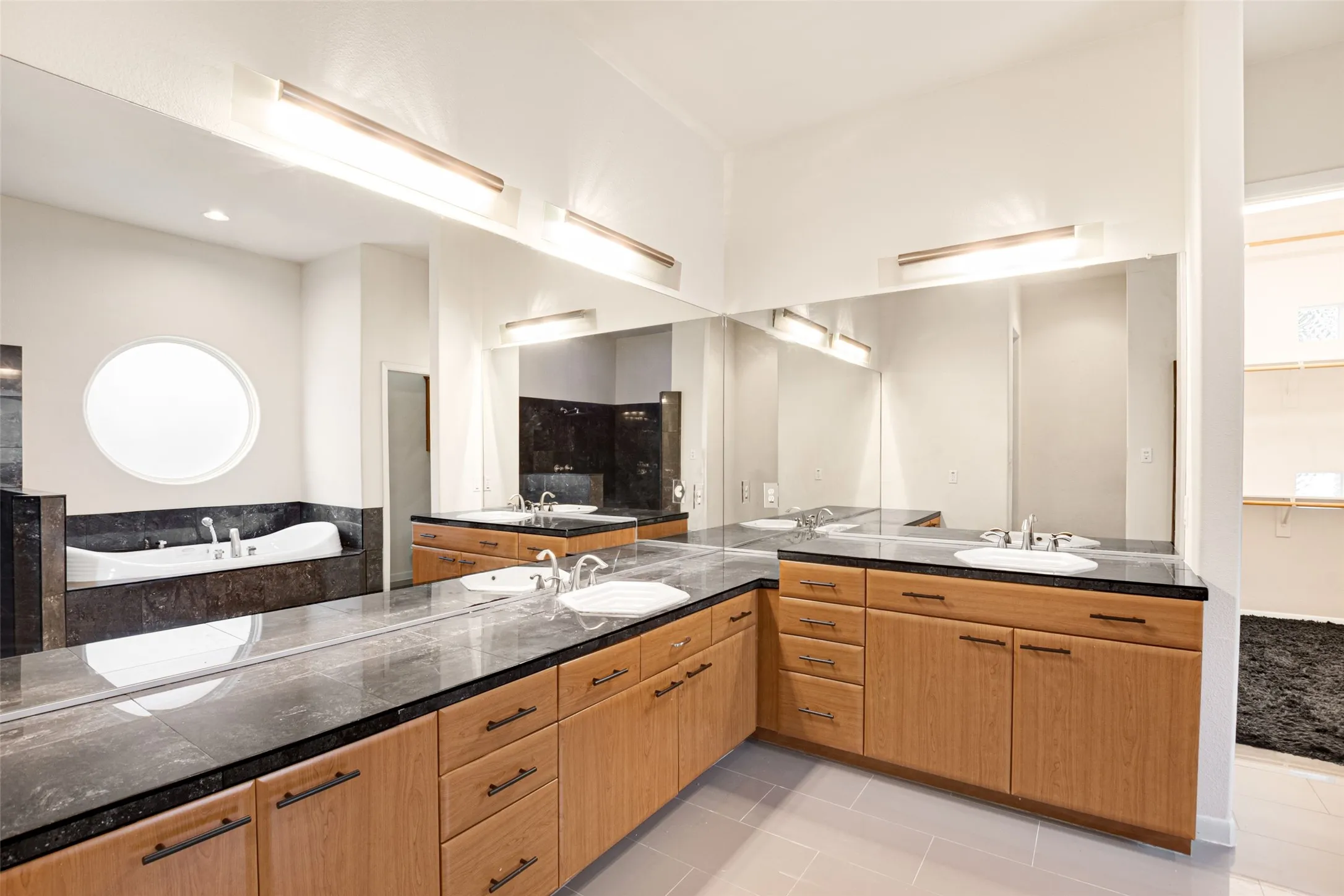 Spa-inspired primary bathroom featuring dual wood-finish vanities with dark stone countertops, vessel sinks, and polished chrome fixtures