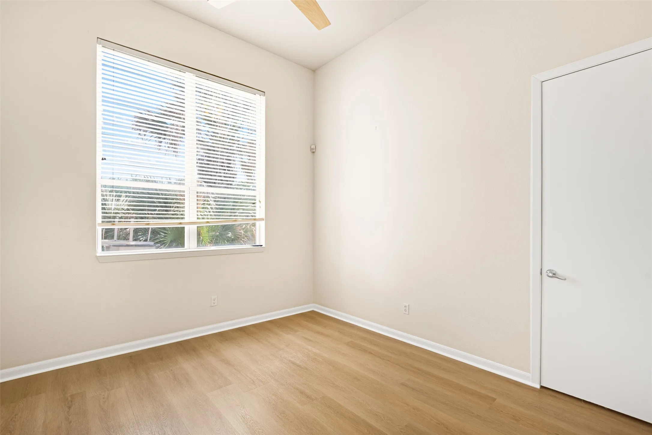 Bright, light-filled bedroom with large dual-pane window, white painted walls, wood-finish flooring, and white interior door trim