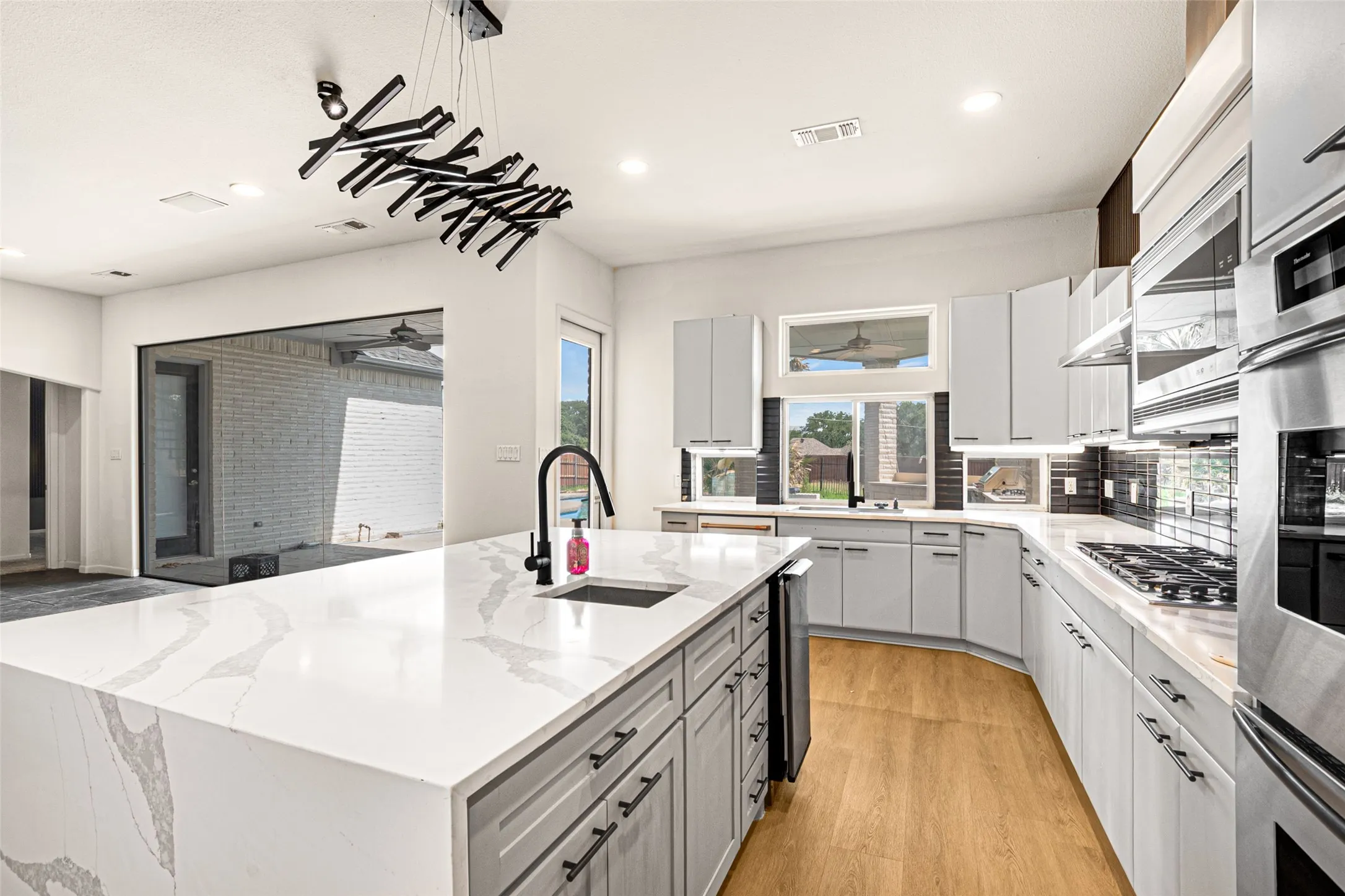 Gourmet kitchen featuring a large center island with waterfall-edge quartz countertop, dual-bowl undermount sink with pull-down faucet, stainless steel gas cooktop, built-in wall ovens, custom cabinetry with soft-close drawers, and abundant recessed lighting