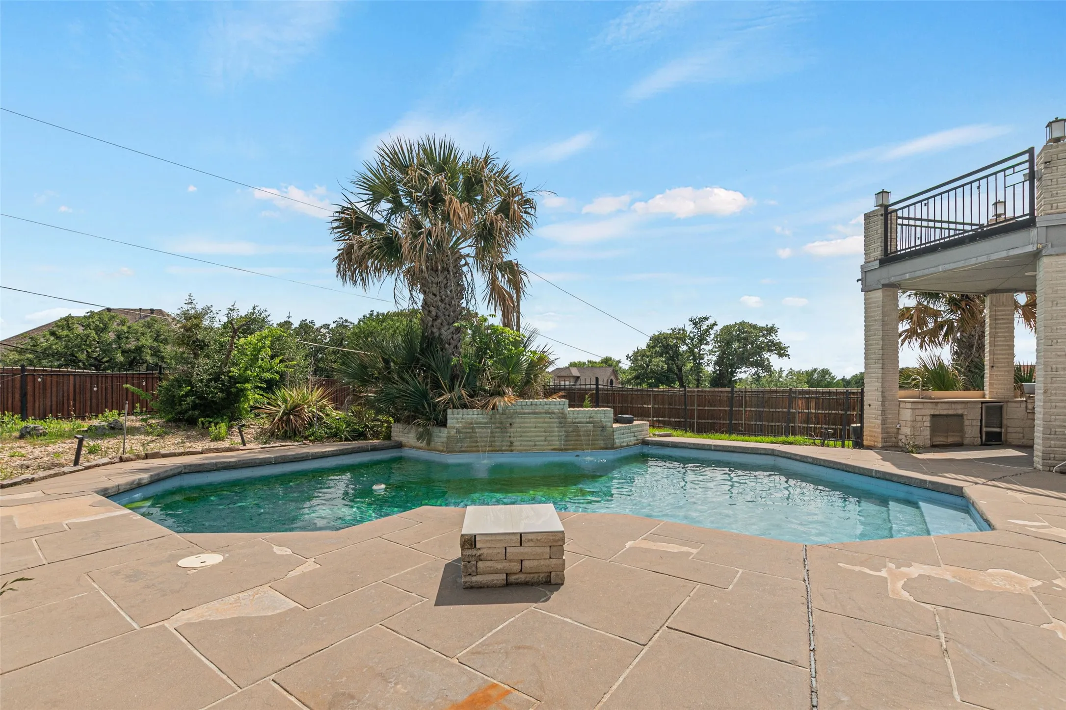 Resort-style backyard oasis featuring a custom free-form swimming pool with stone decking, mature palm tree, integrated spa, and elevated covered lounge pavilion with stone columns overlooking the grounds