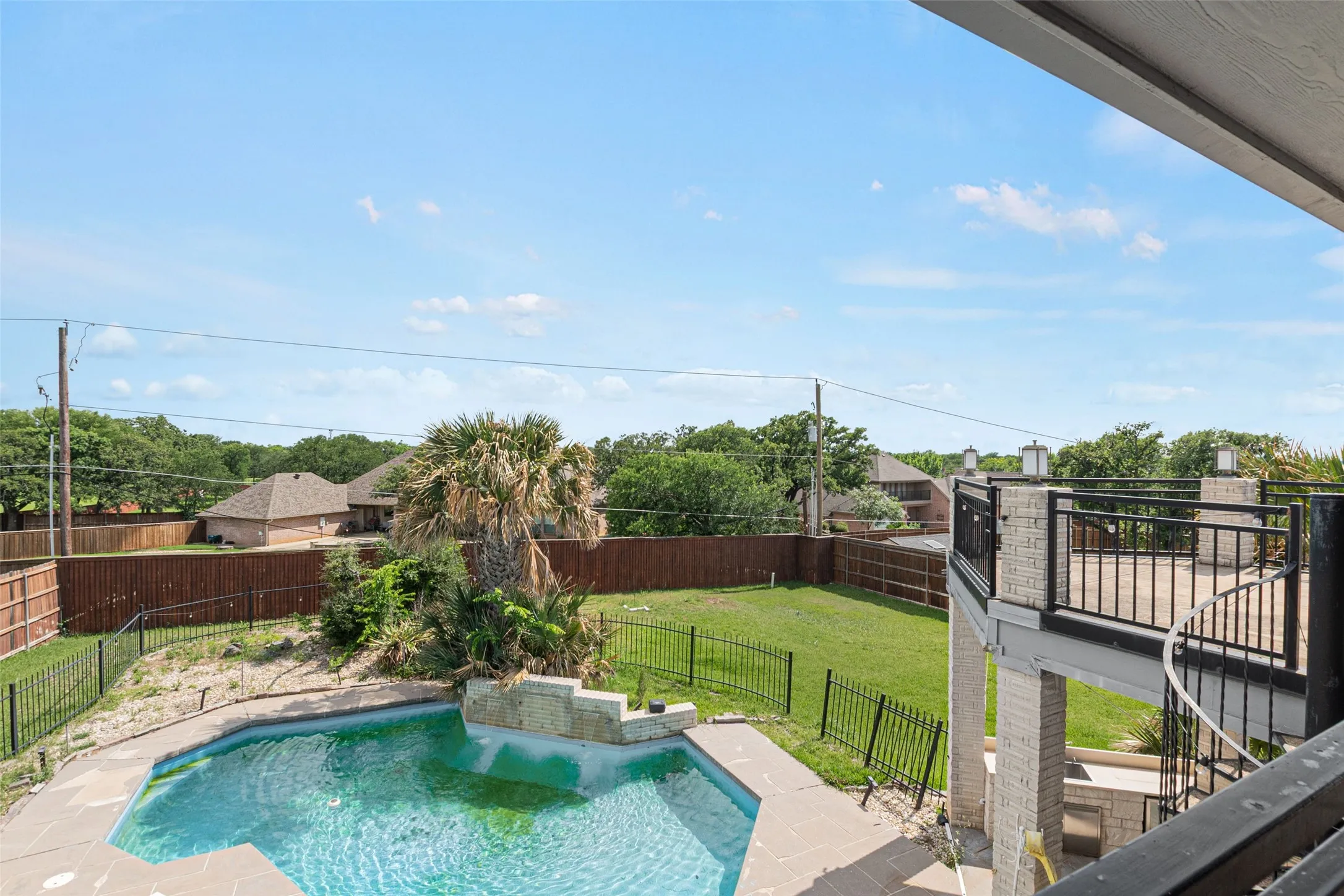 Expansive backyard oasis featuring a resort-style swimming pool with curved edges and integrated spa, surrounded by black metal fencing and manicured lawn