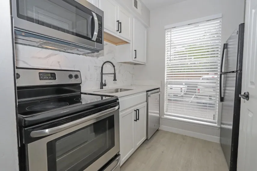 Galley kitchen featuring stainless steel appliances, white cabinetry with hardware accents, quartz countertops, a pull-down faucet at the sink, and wood-finish flooring throughout