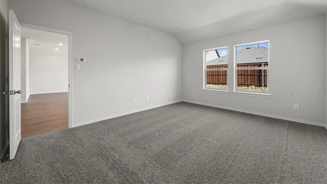 Bright, light-filled bedroom showcasing neutral wall finishes, expansive windows with natural light, neutral carpet flooring, and a white entry door with hardware