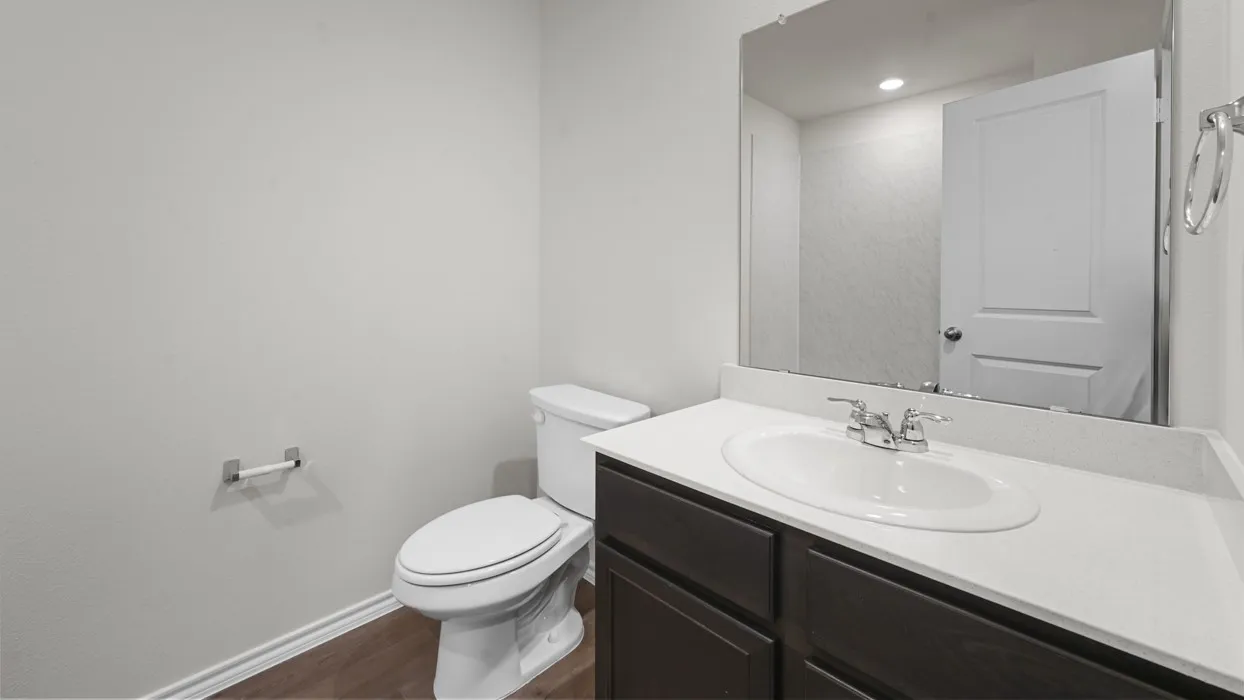Modern bathroom featuring a dark wood vanity with dual-sink white countertop, polished chrome faucet, and large framed mirror with integrated lighting