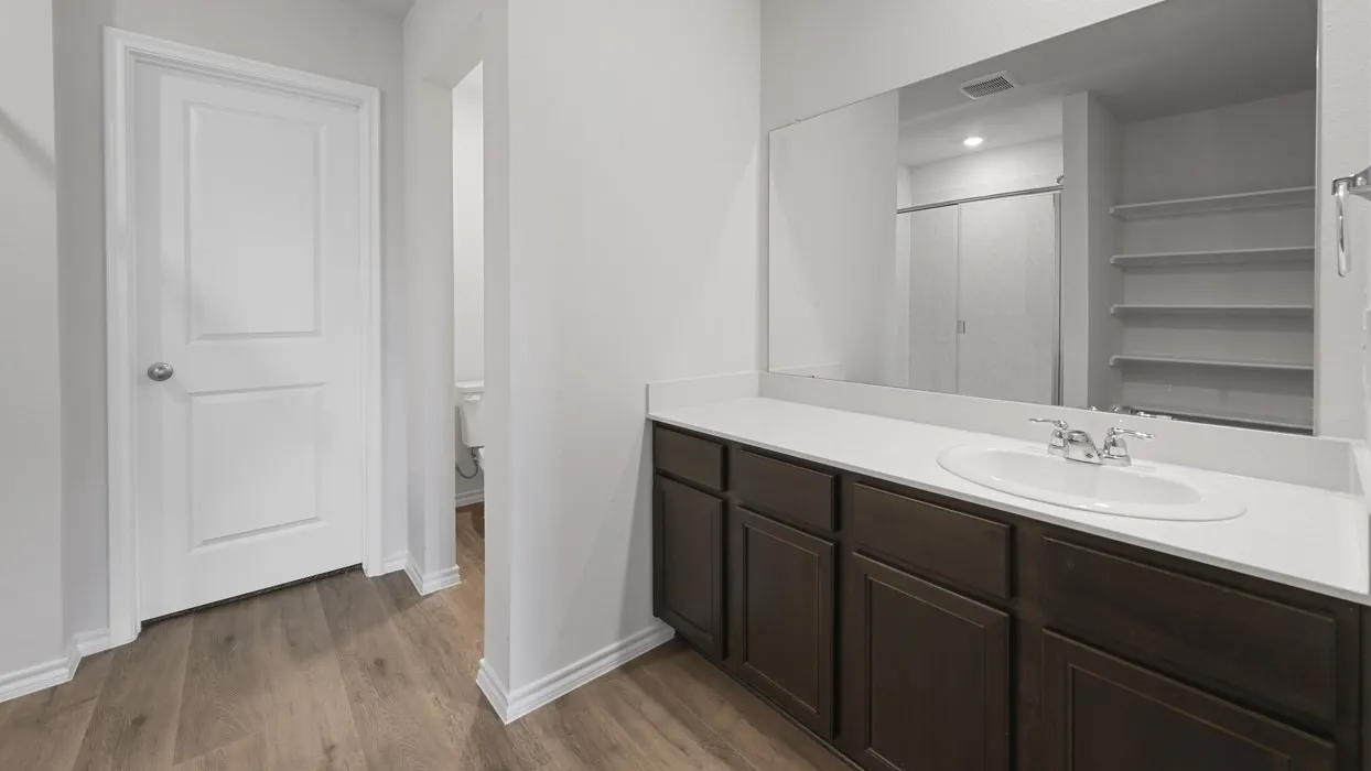 Spa-inspired primary bathroom featuring a dark wood vanity with ample storage, white quartz countertop, and an expansive framed mirror with integrated lighting