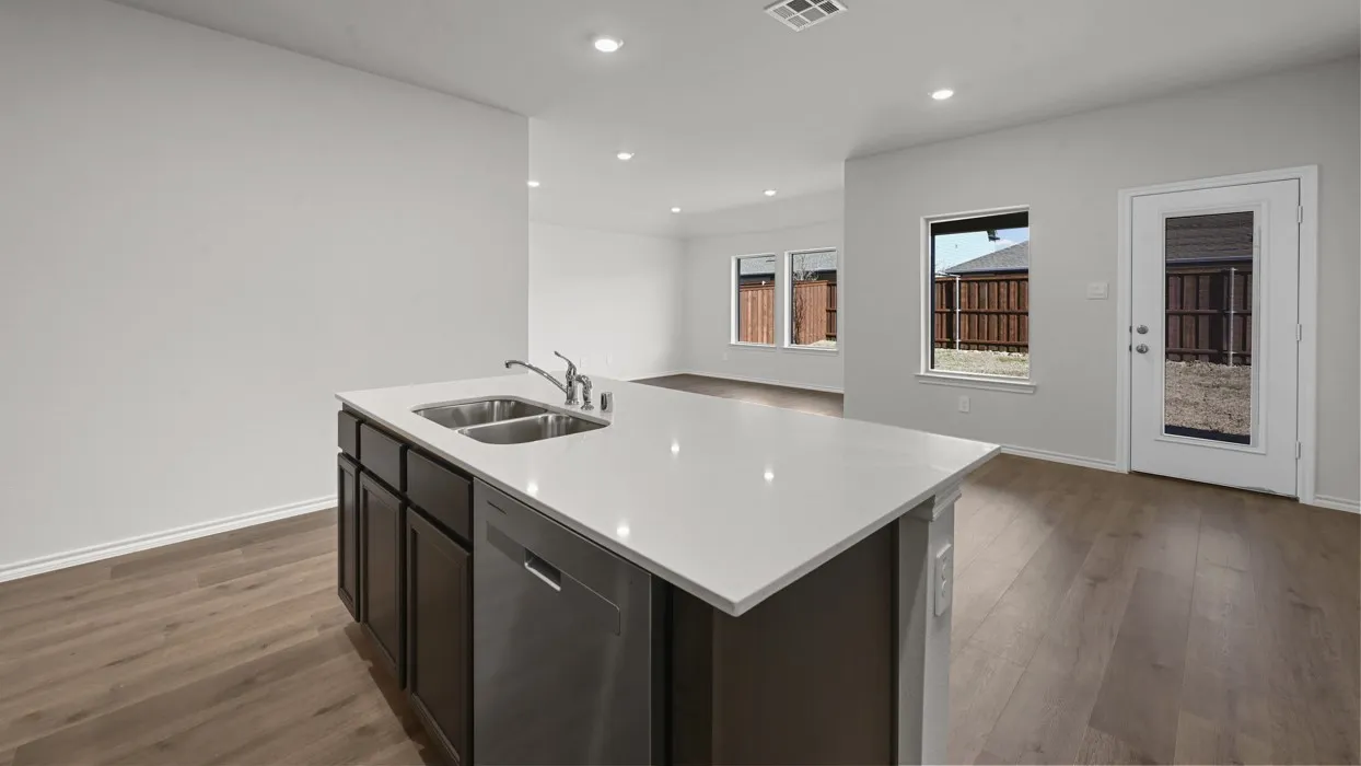 Modern kitchen island with white quartz countertop and dark cabinetry featuring integrated appliances, stainless steel sink with faucet, and ample counter space