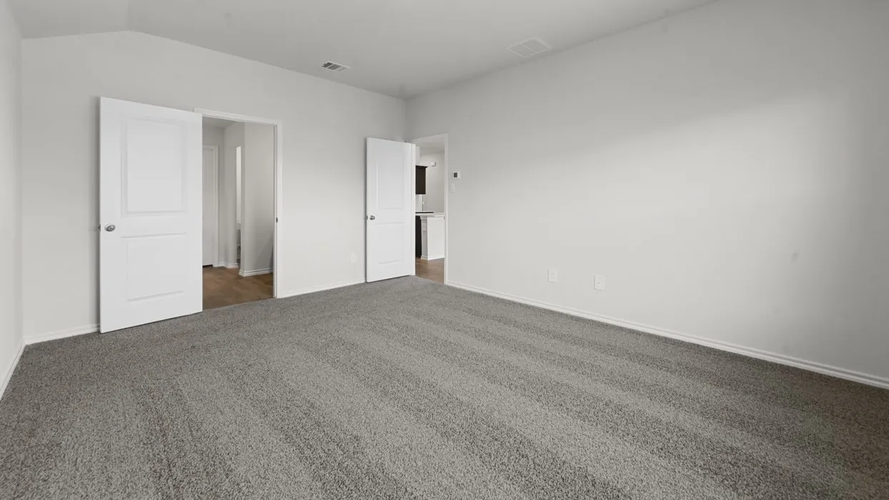 Spacious bedroom featuring neutral wall finishes, gray carpet flooring, and multiple white six-panel closet doors providing ample storage and natural room proportions