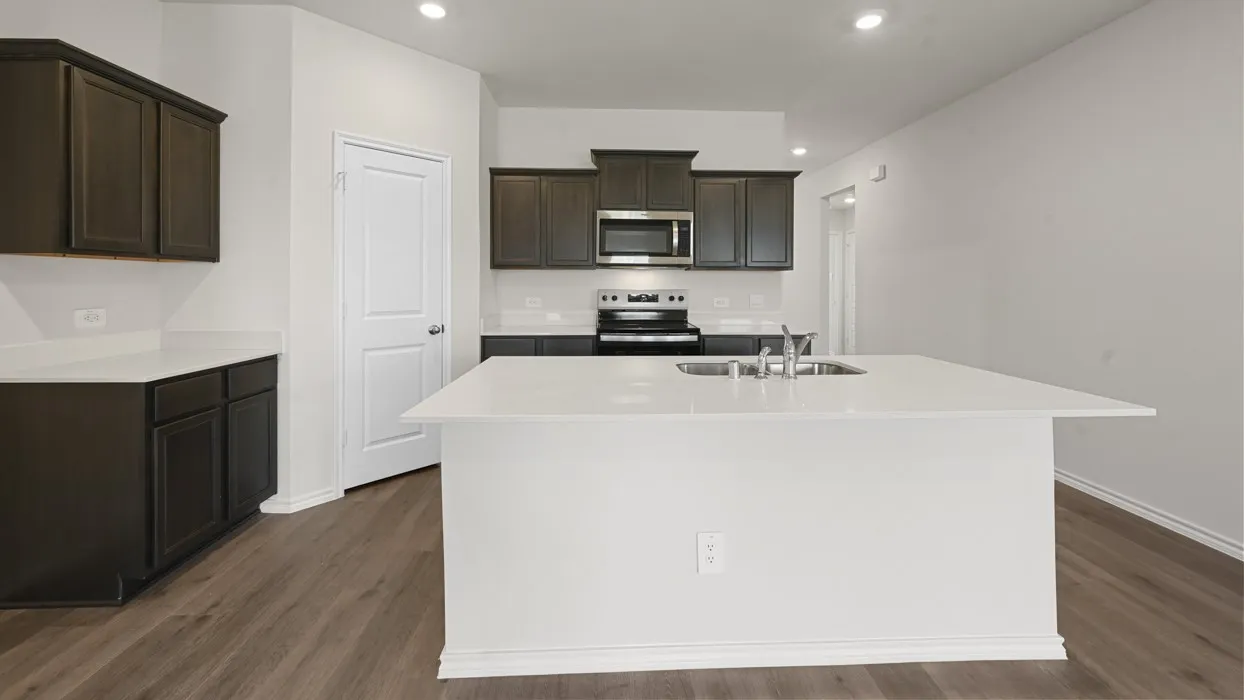 Modern kitchen featuring dark cabinetry with stainless steel appliances, a spacious white quartz island with seating, wood-finish flooring throughout, recessed ceiling lighting, and an open-concept layout with ample counter workspace