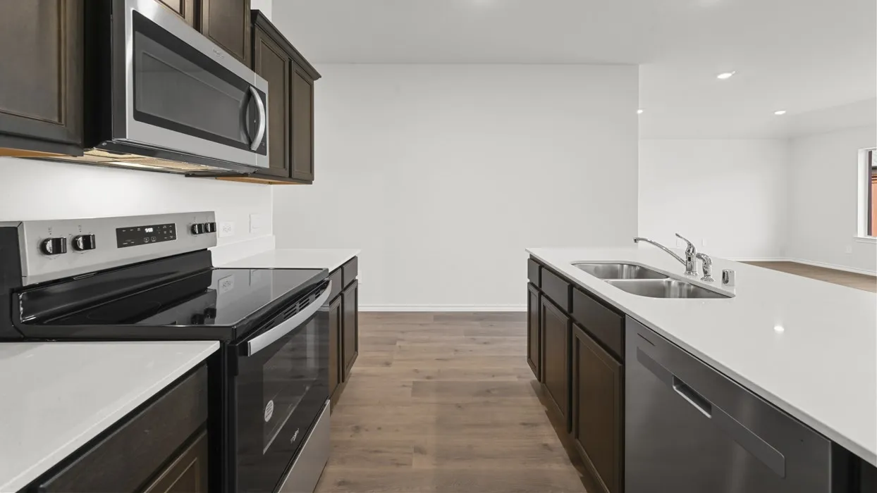 Modern galley kitchen featuring dark cabinetry with stainless steel appliances, white quartz countertops, an undermount sink with chrome faucet, wood-finish flooring, and ample counter workspace across dual work stations