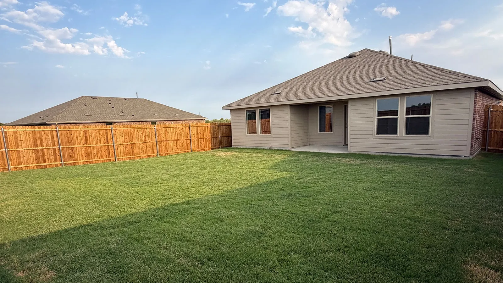 Expansive backyard with a manicured lawn, full privacy fencing, and a concrete patio