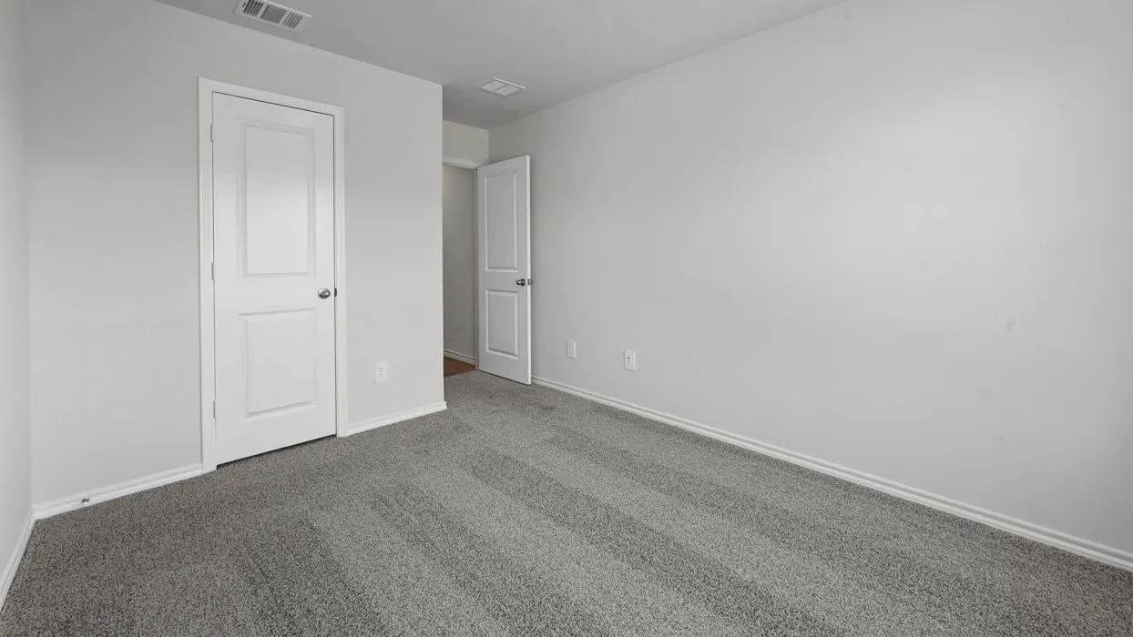 Spacious bedroom featuring neutral wall finishes, gray carpeting, and dual white six-panel doors providing practical entry and closet access