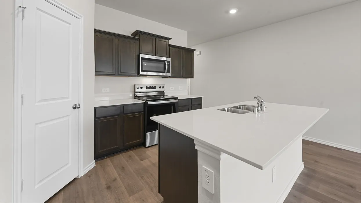 Modern kitchen featuring dark cabinetry with stainless steel appliances, white quartz countertops, a spacious island with seating, undermount sink with chrome faucet, and wood-finish flooring throughout