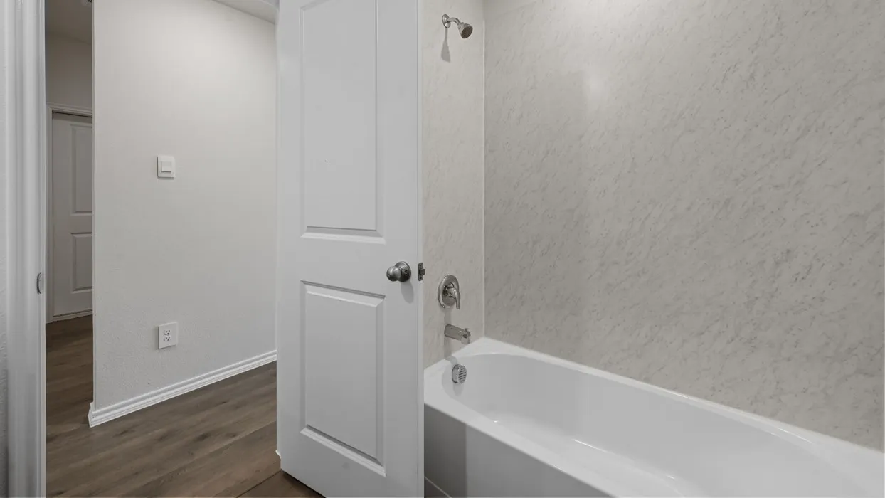 Modern bathroom featuring a soaking tub with integrated surround, marble-look wall tile, wood-finish flooring, chrome fixtures, and direct access to the hallway