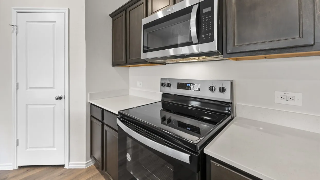 Kitchen with wood-finish flooring, dark wood cabinetry, light-toned countertops, stainless steel appliances, and a white paneled door