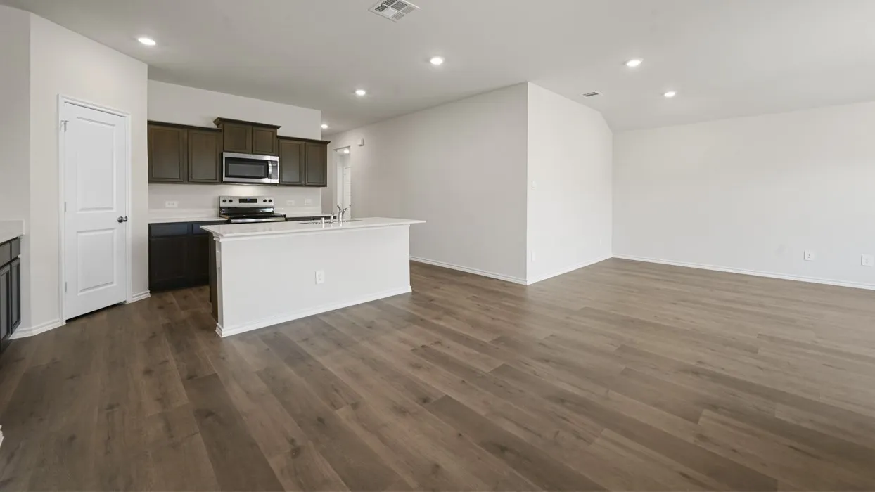 Open-concept living space featuring wood-finish flooring throughout, a white quartz island with waterfall countertop edge, stainless steel appliances, dark cabinetry with integrated hardware, recessed ceiling lighting, and abundant natural light from multiple windows
