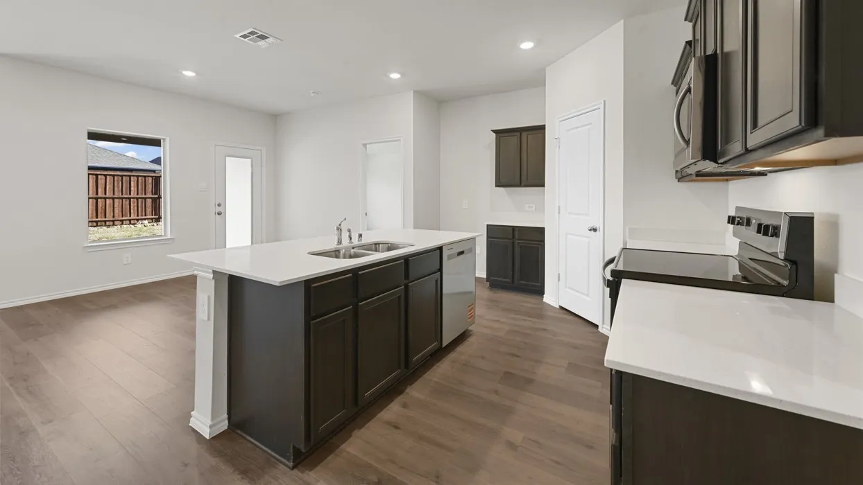 Modern kitchen featuring a large center island with dark cabinetry and white quartz countertops, stainless steel appliances including a wall-mounted microwave, wood-finish flooring throughout, and recessed ceiling lighting