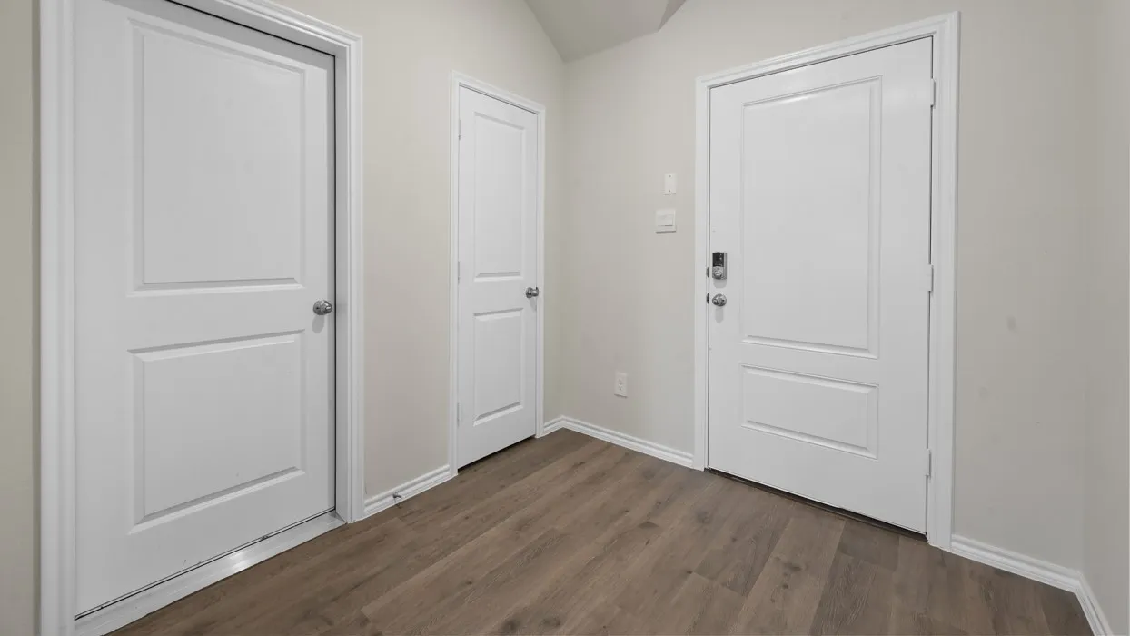 Bright foyer showcasing multiple white six-panel doors, warm wood-finish flooring, and clean white walls with neutral trim throughout