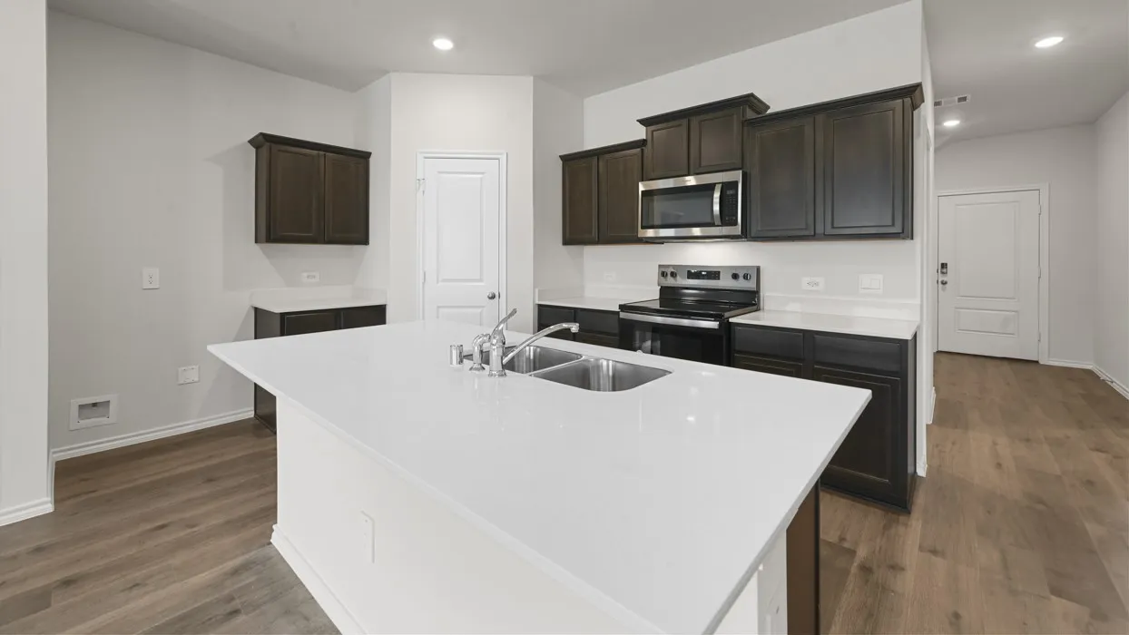 Modern kitchen featuring a large white quartz-finish island with undermount sink, dark cabinetry throughout, stainless steel appliances including a built-in microwave, wood-finish flooring, and recessed ceiling lighting
