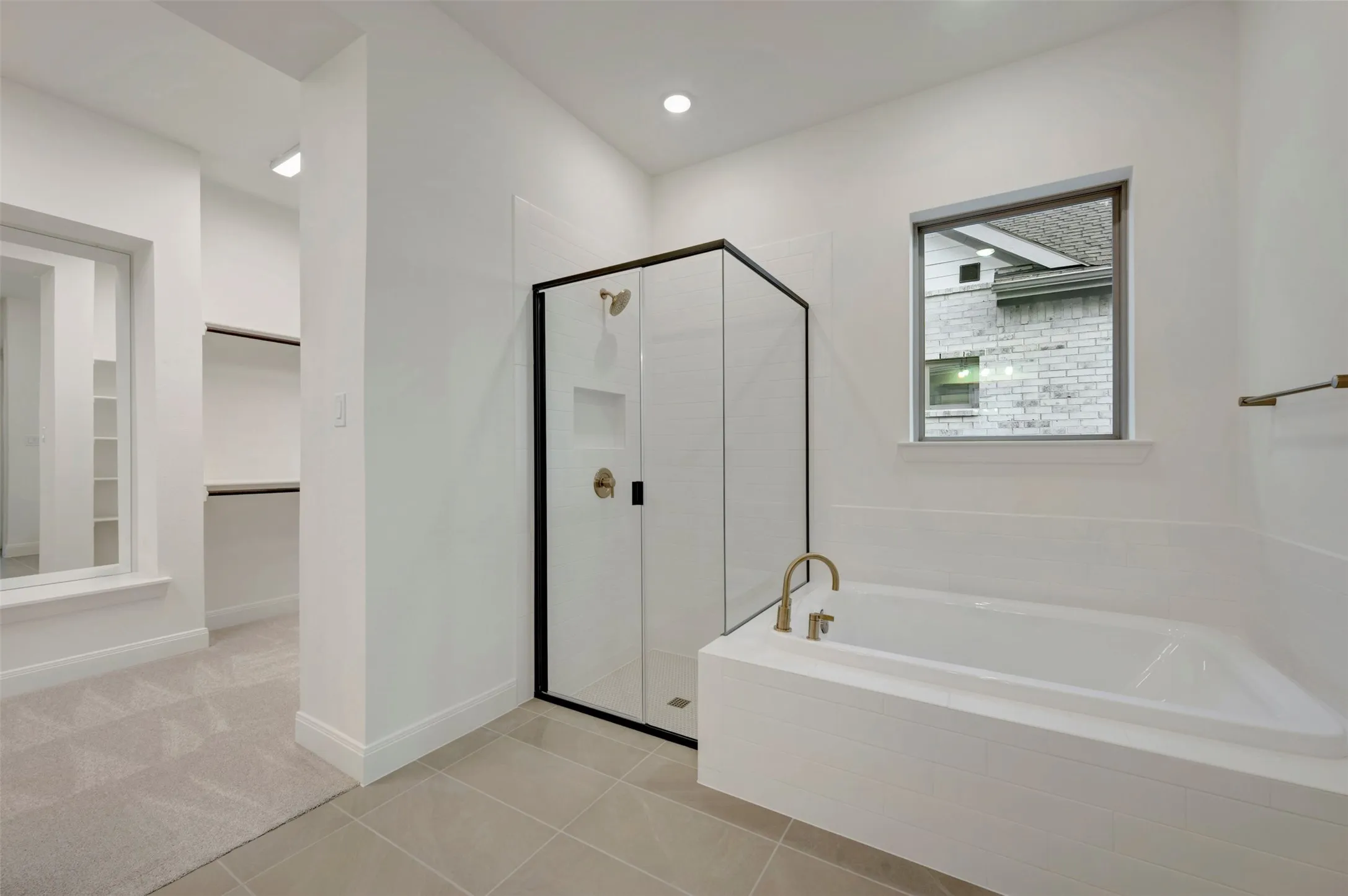 Soaking tub with brass-finish fixtures, glass-enclosed shower with black trim, and tile flooring