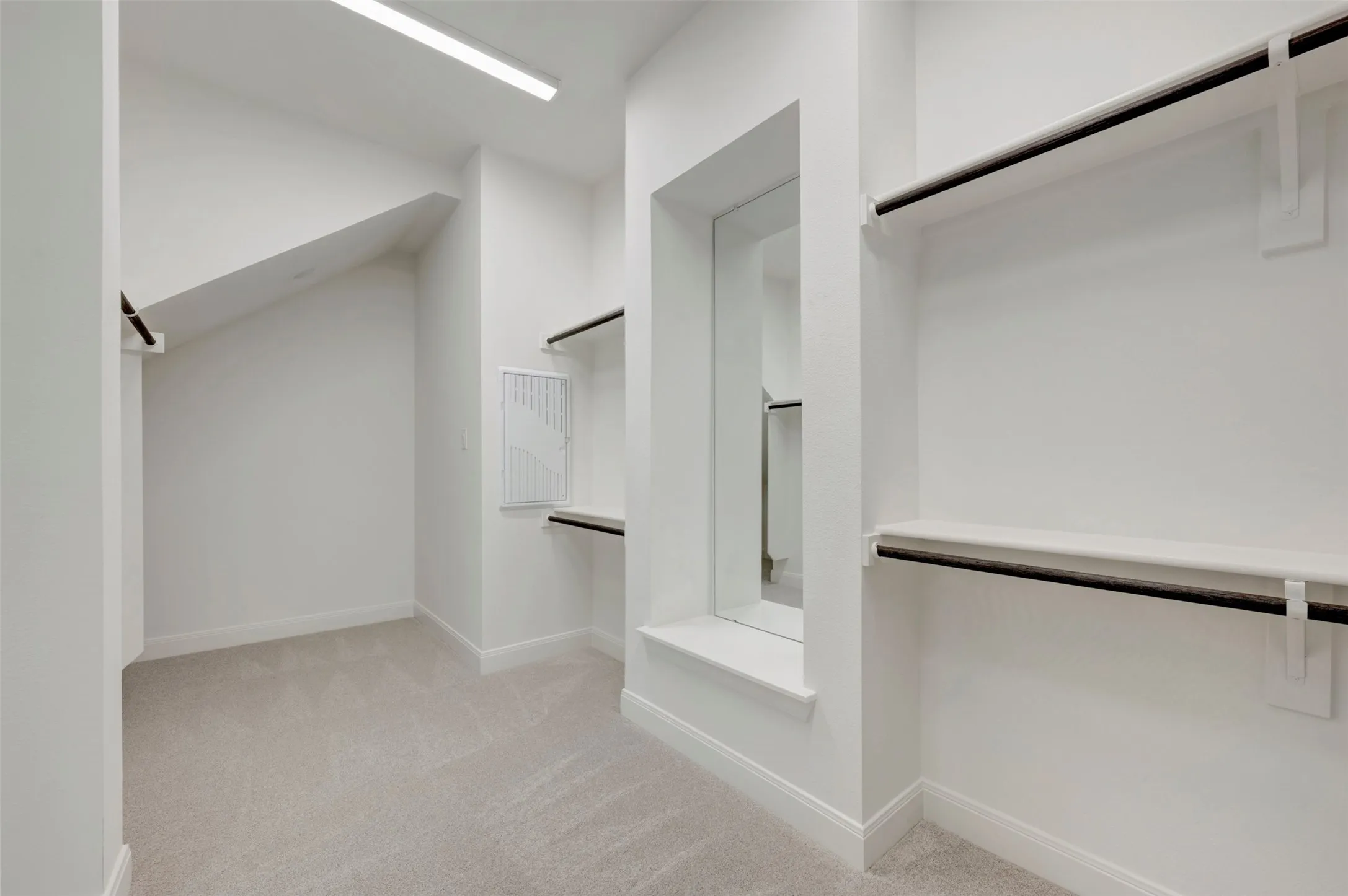 Recessed lighting, light gray carpet, multiple built-in shelving units, integrated hanging rods, and a full-length mirror