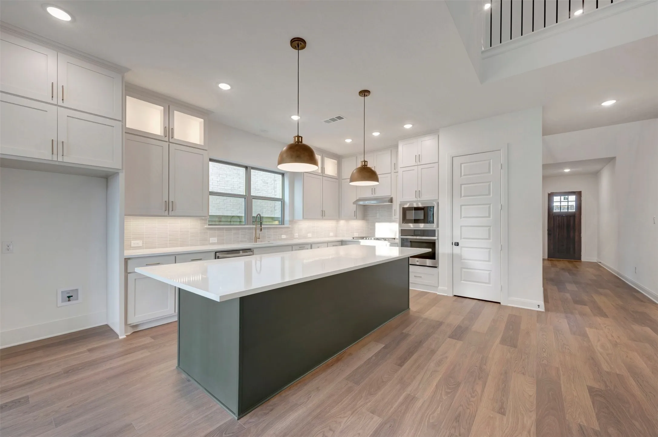 Kitchen featuring a large island with a light-toned countertop, white cabinetry with bronze hardware, and wood-finish flooring