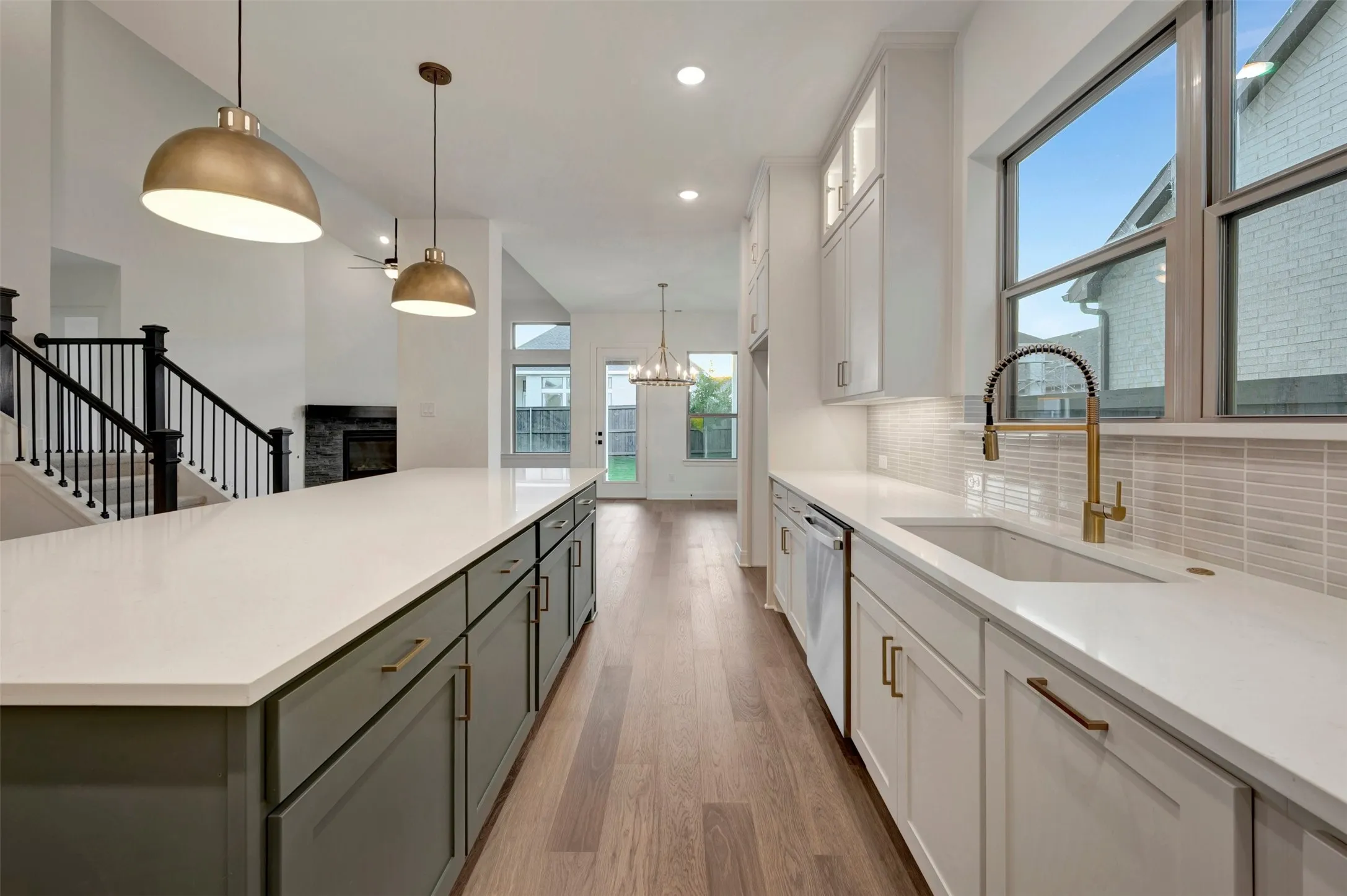 Spacious kitchen island with white countertop, brass pendant lighting, wood-finish flooring, white cabinetry, and a subway tile backsplash