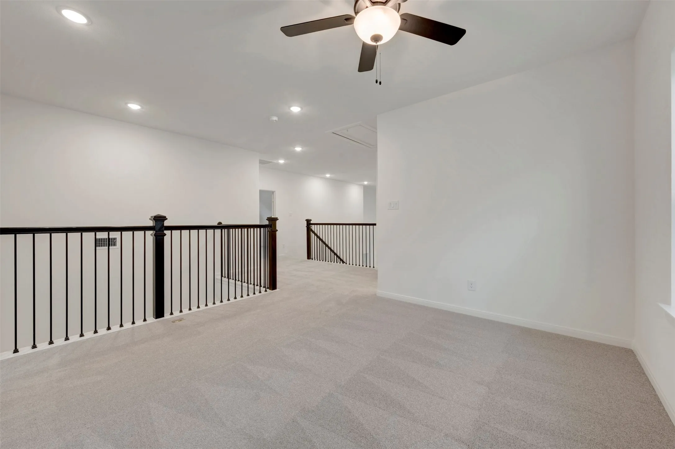 Carpeted open loft area featuring a ceiling fan with integrated lighting, recessed lighting, and black metal balusters with wood newel posts