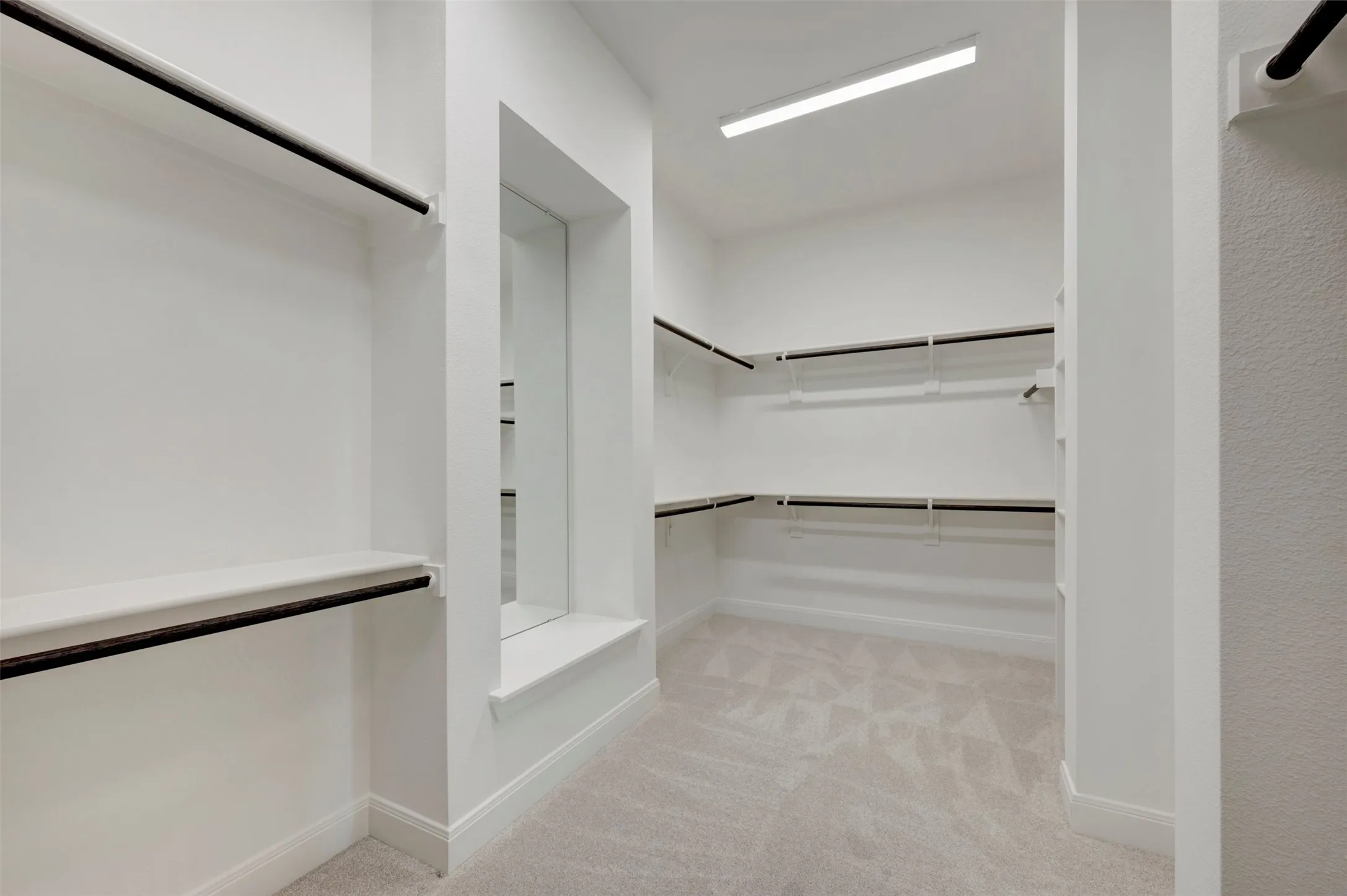 Walk-in closet featuring extensive built-in shelving, multiple hanging rods, recessed mirror, and soft pile carpeting