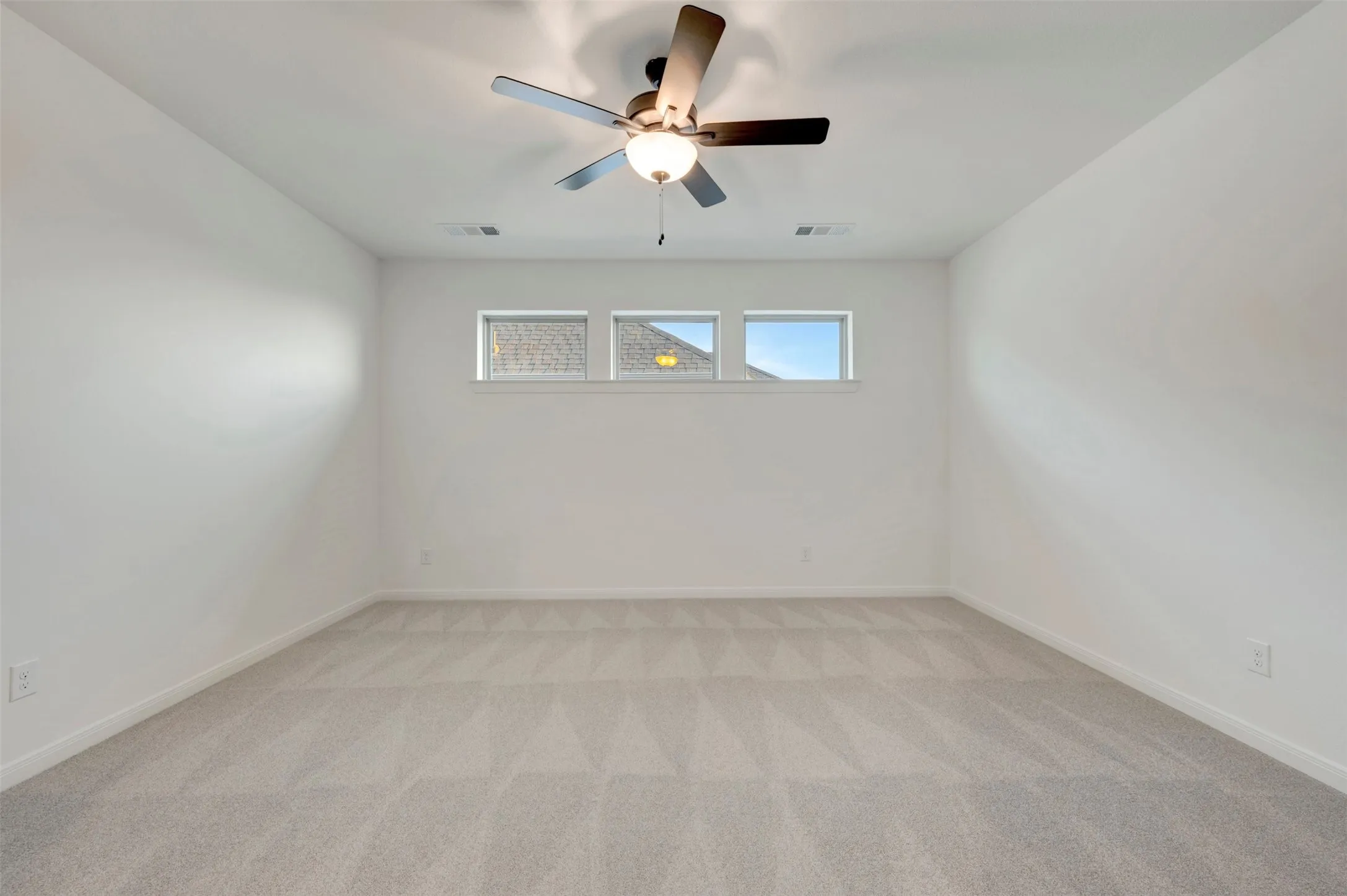 Expansive room featuring light gray carpeting, neutral wall paint, and a ceiling fan with integrated lighting