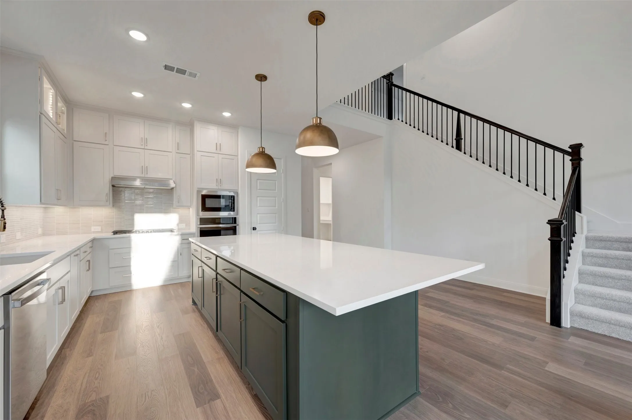 Kitchen featuring a large central island with a solid surface countertop, wood-finish flooring, white cabinetry, and stainless steel appliances