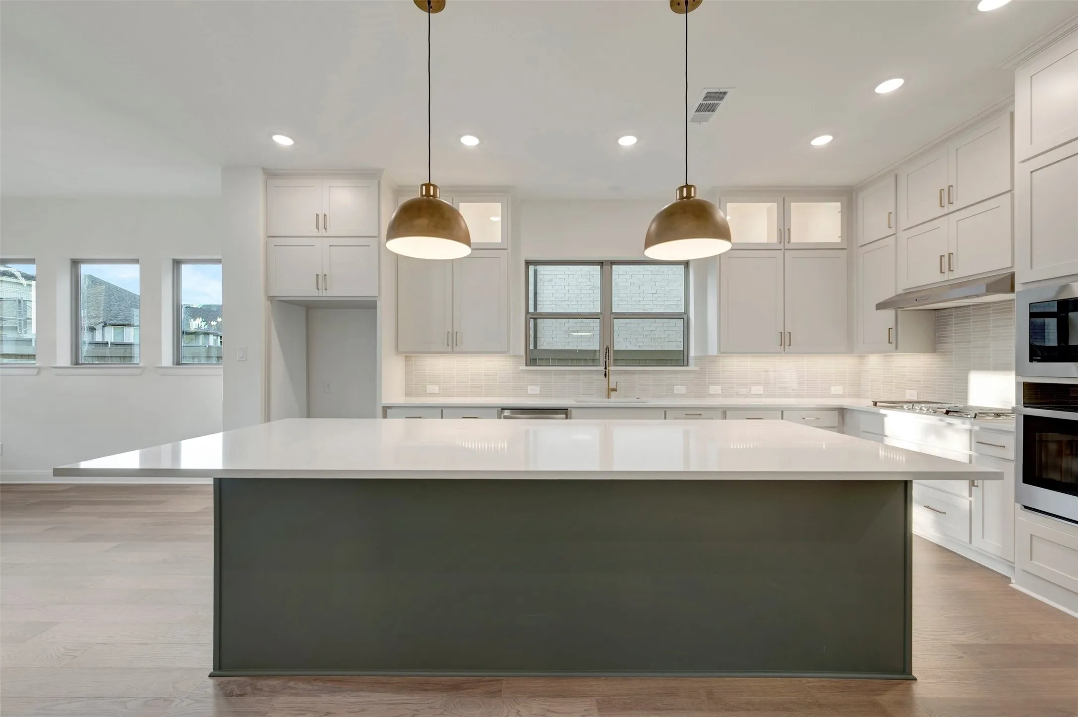 Spacious kitchen featuring a large central island with a solid surface countertop, white cabinetry, integrated stainless steel appliances, and wood-finish flooring