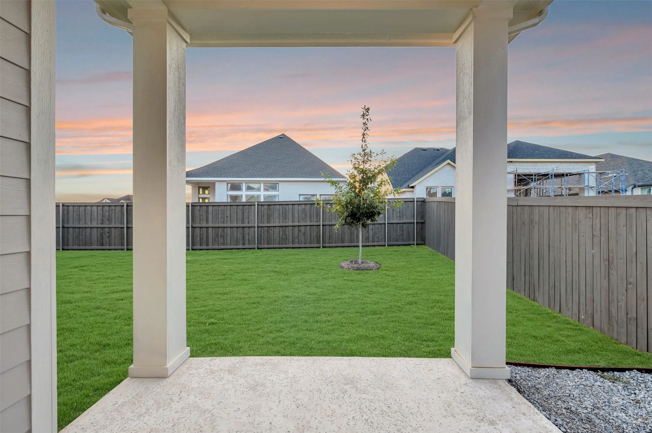 Covered patio with a concrete surface, leading to a manicured lawn and a privacy fence